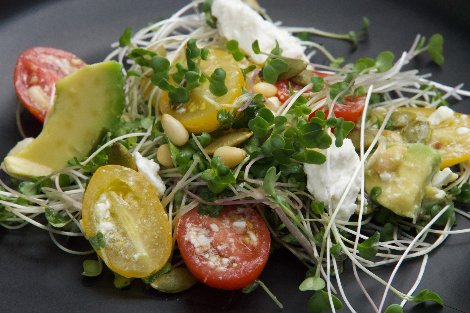 A plate of microgreens with heirloom tomato, avocado and pine nuts