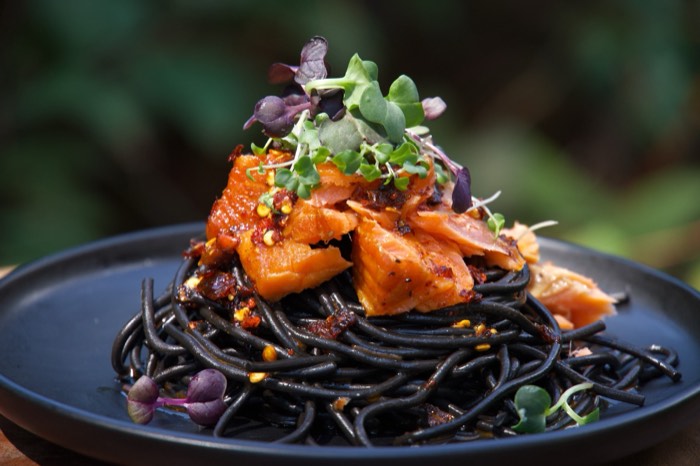 Squid ink pasta with salmon and microgreens on a dark plate